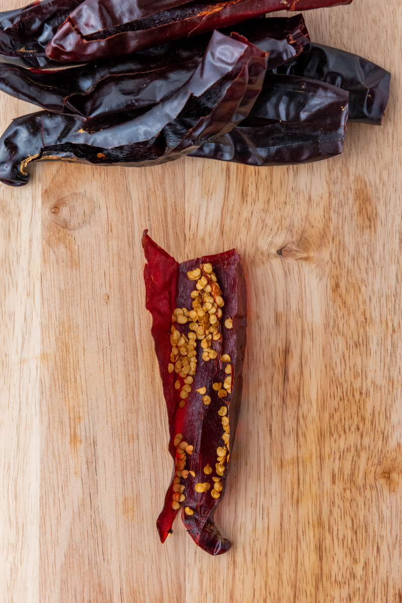 Dried guajillo chili with seeds exposed on wooden cutting board.