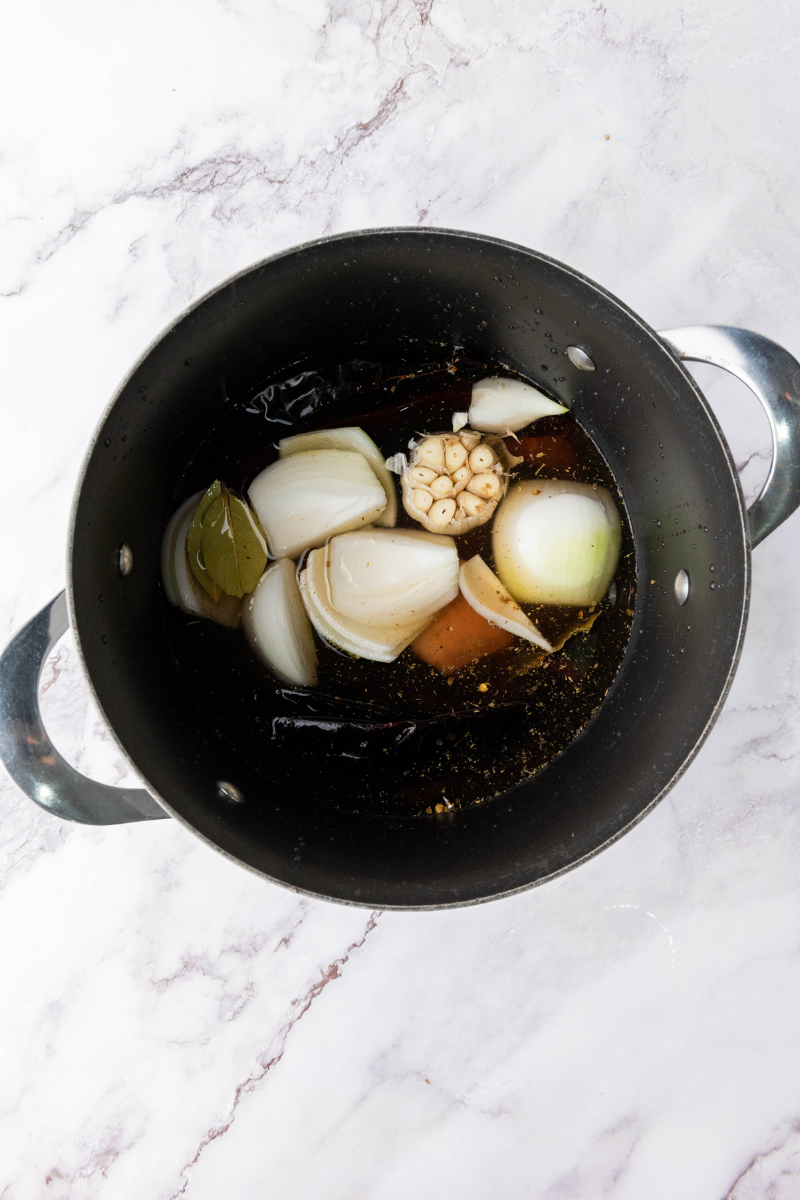 Birria ingredients simmering in broth inside large cooking pot.