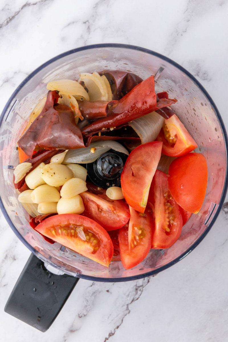 Cooked chilies, tomatoes, onions, and garlic inside blender for birria sauce.