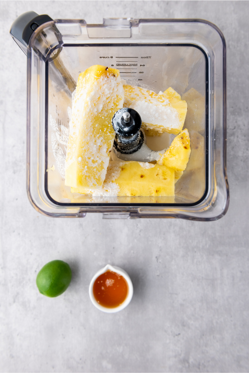 Pineapple chunks in a blender with coconut milk and honey for tropical popsicles.