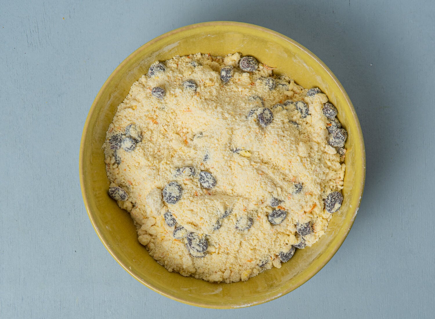 Dried cranberries folded into orange scone dough in a mixing bowl.