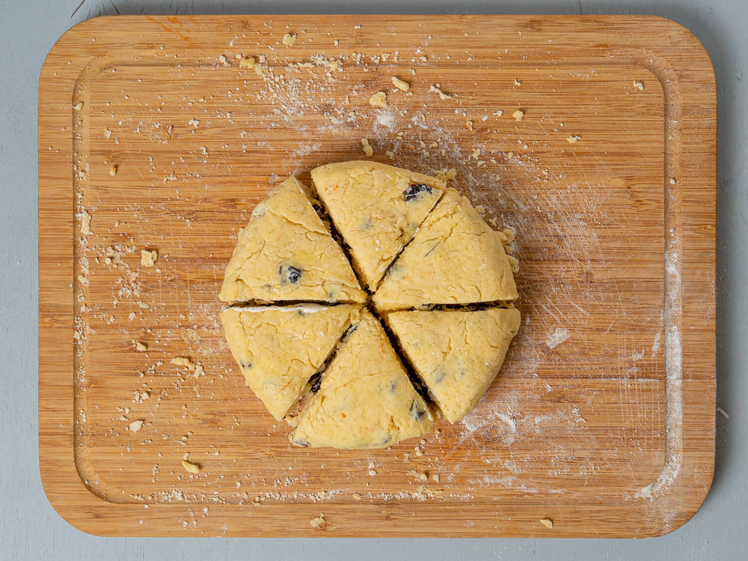 Round orange cranberry scone dough cut into six triangular wedges on a floured wooden board.