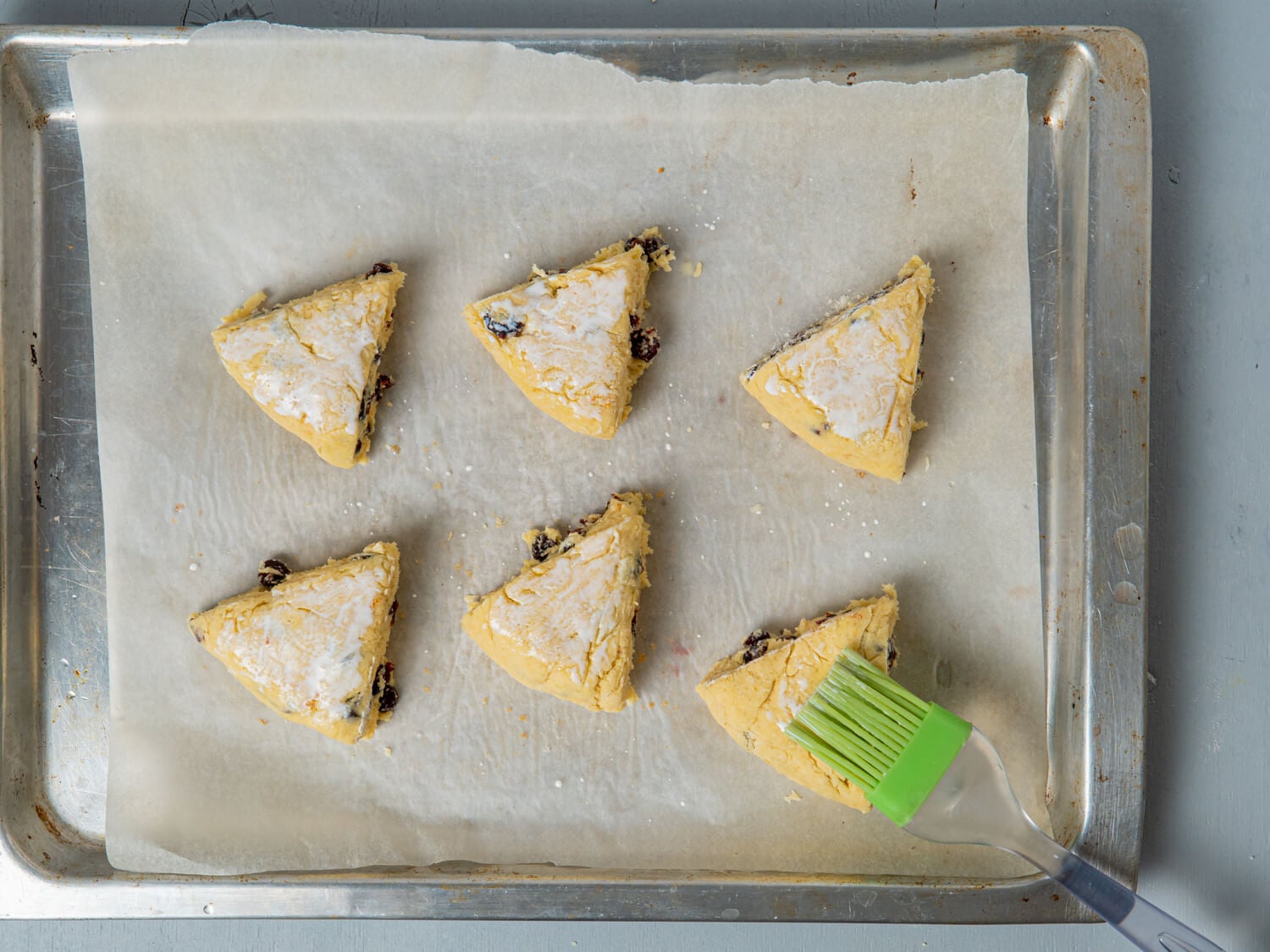 Six triangular orange cranberry scones arranged on a parchment-lined baking sheet.