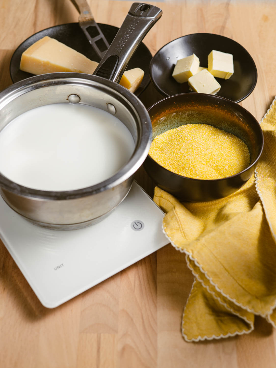 Saucepan with milk beside coarse-ground polenta, butter, and Parmesan cheese.