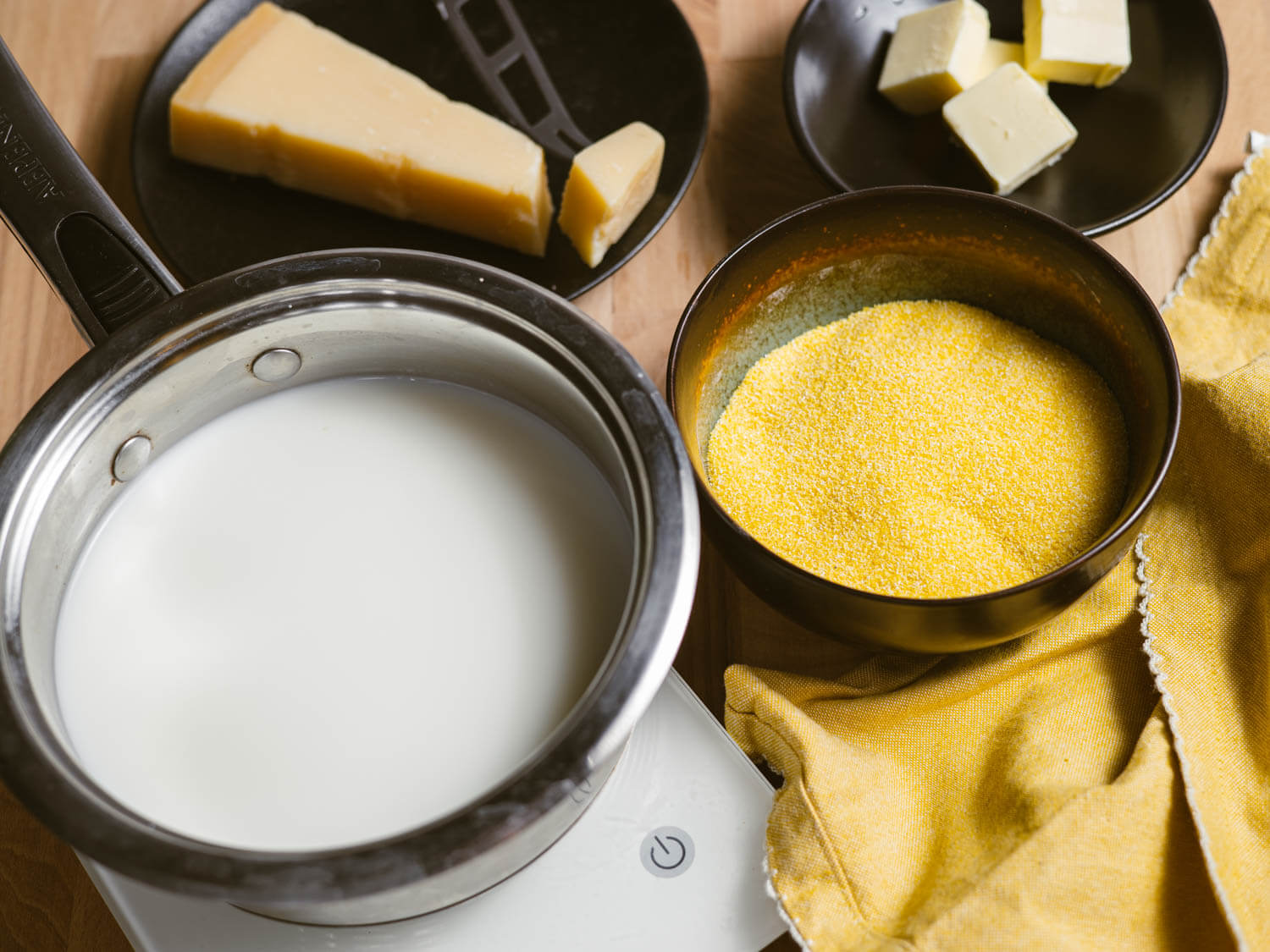 Saucepan of milk beside a bowl of coarse-ground polenta for making creamy Parmesan polenta.

