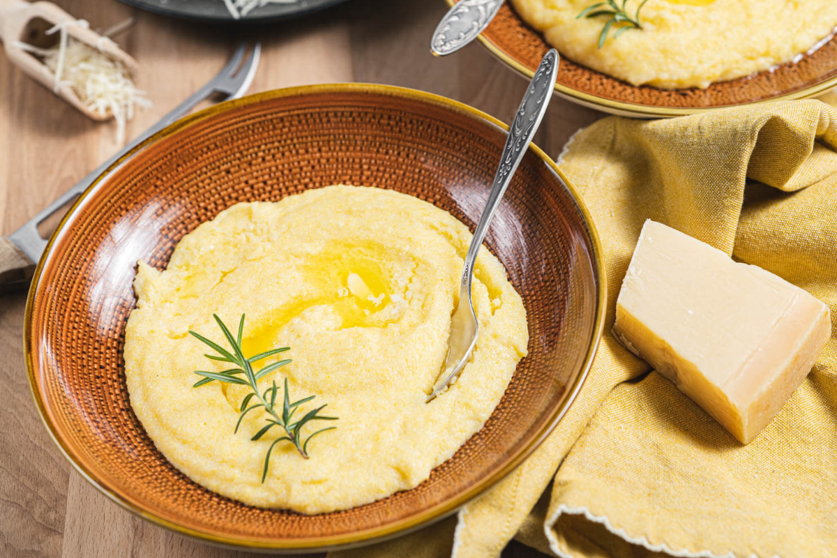 Coarse-ground polenta, Parmesan cheese, butter, and cookware arranged for making creamy Parmesan polenta.