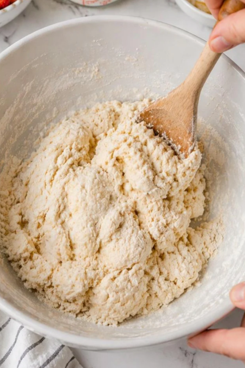 Shaggy biscuit dough being mixed with buttermilk in a large bowl for strawberry shortcake.