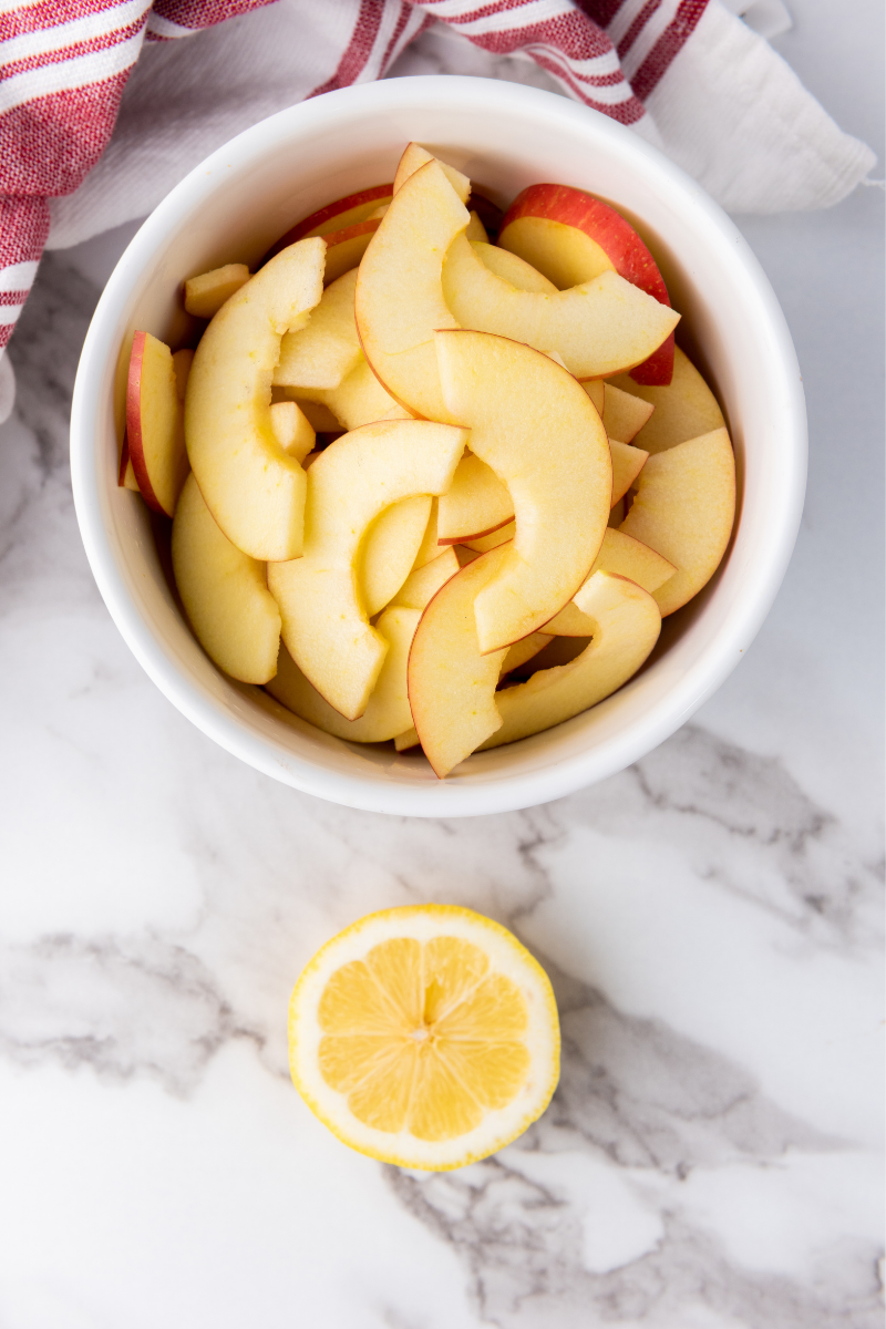 Apple slices in a bowl with fresh lemon for preparing apple rose pastries.