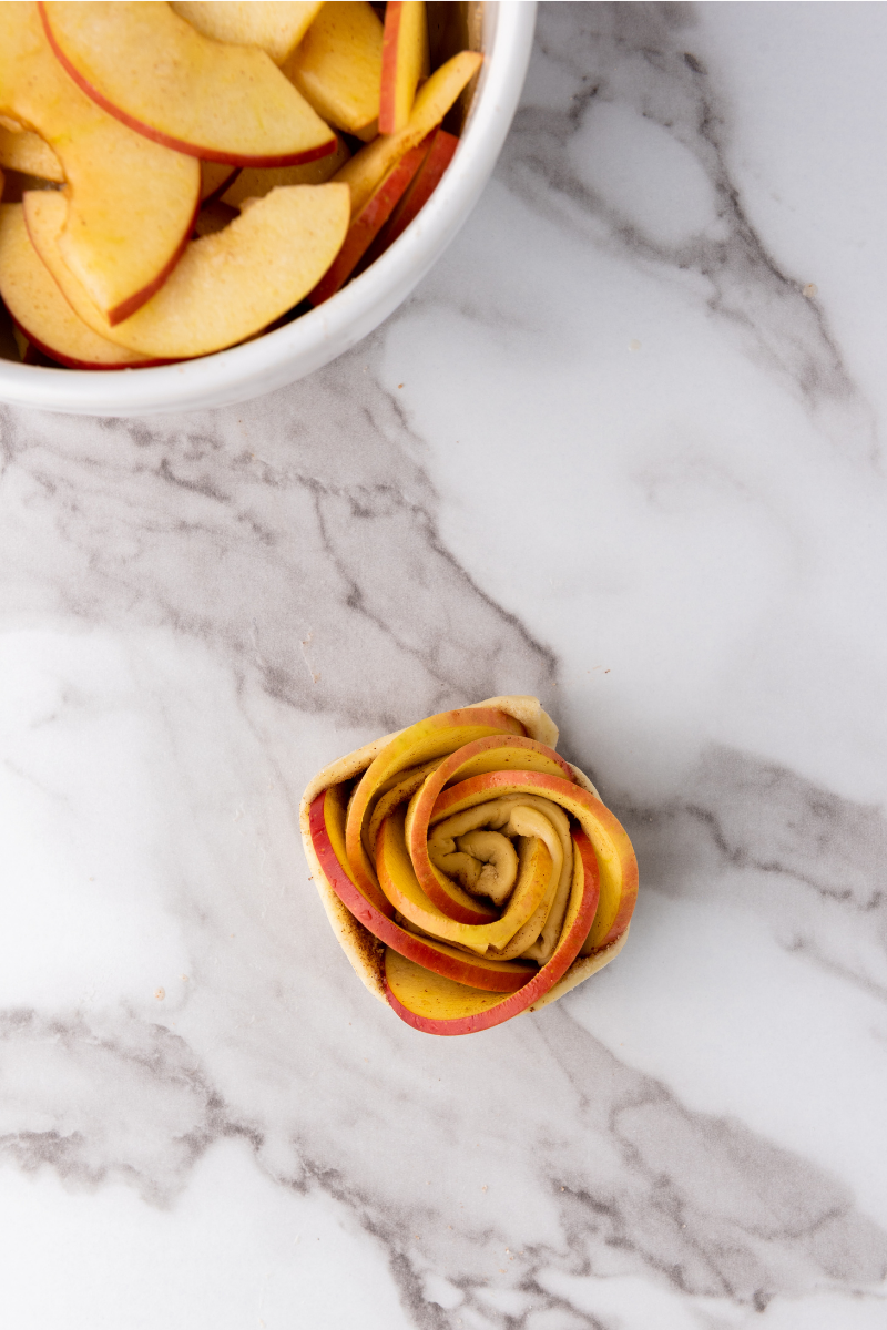 Rolled apple rose puff pastry shaped into a small flower before baking.