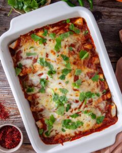 A plate of easy homemade chicken enchiladas topped with cheese, garnished with fresh cilantro and served with a side of salsa