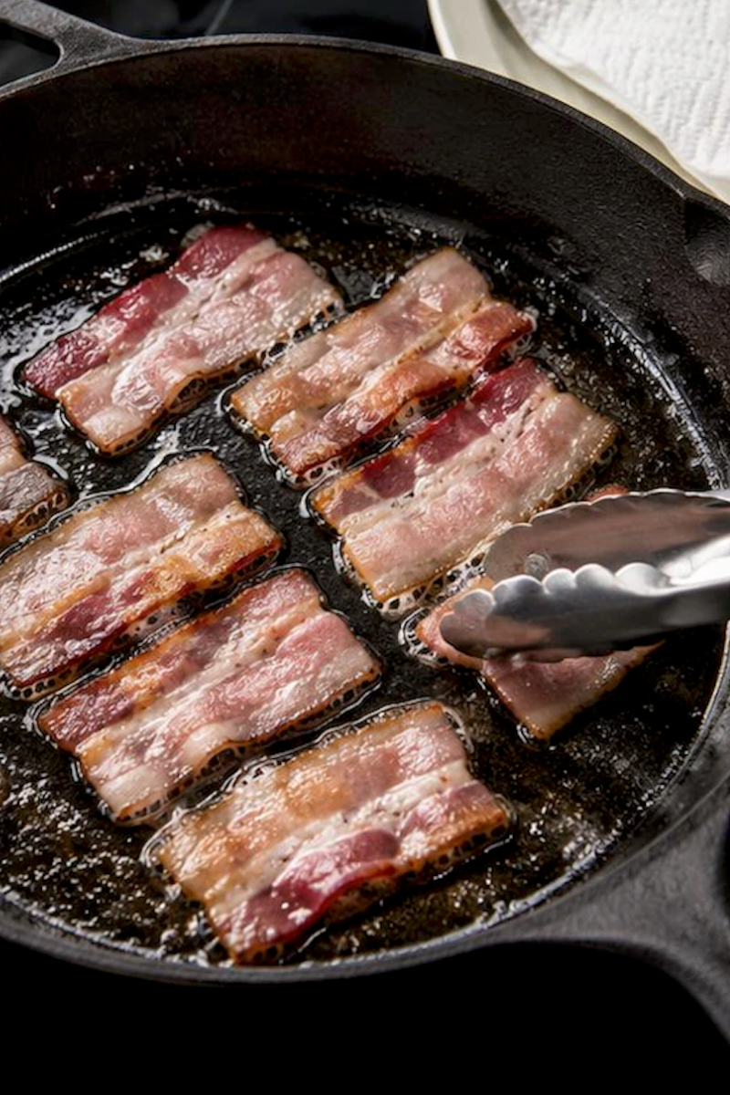 Bacon slices partially cooking in a skillet before being wrapped around scallops