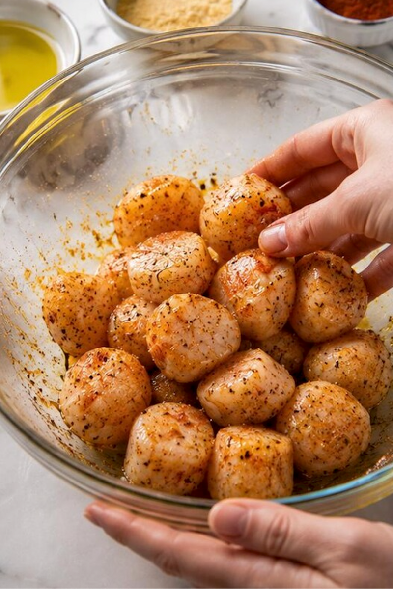 Sea scallops being tossed in a bowl with butter, garlic, paprika and seasonings