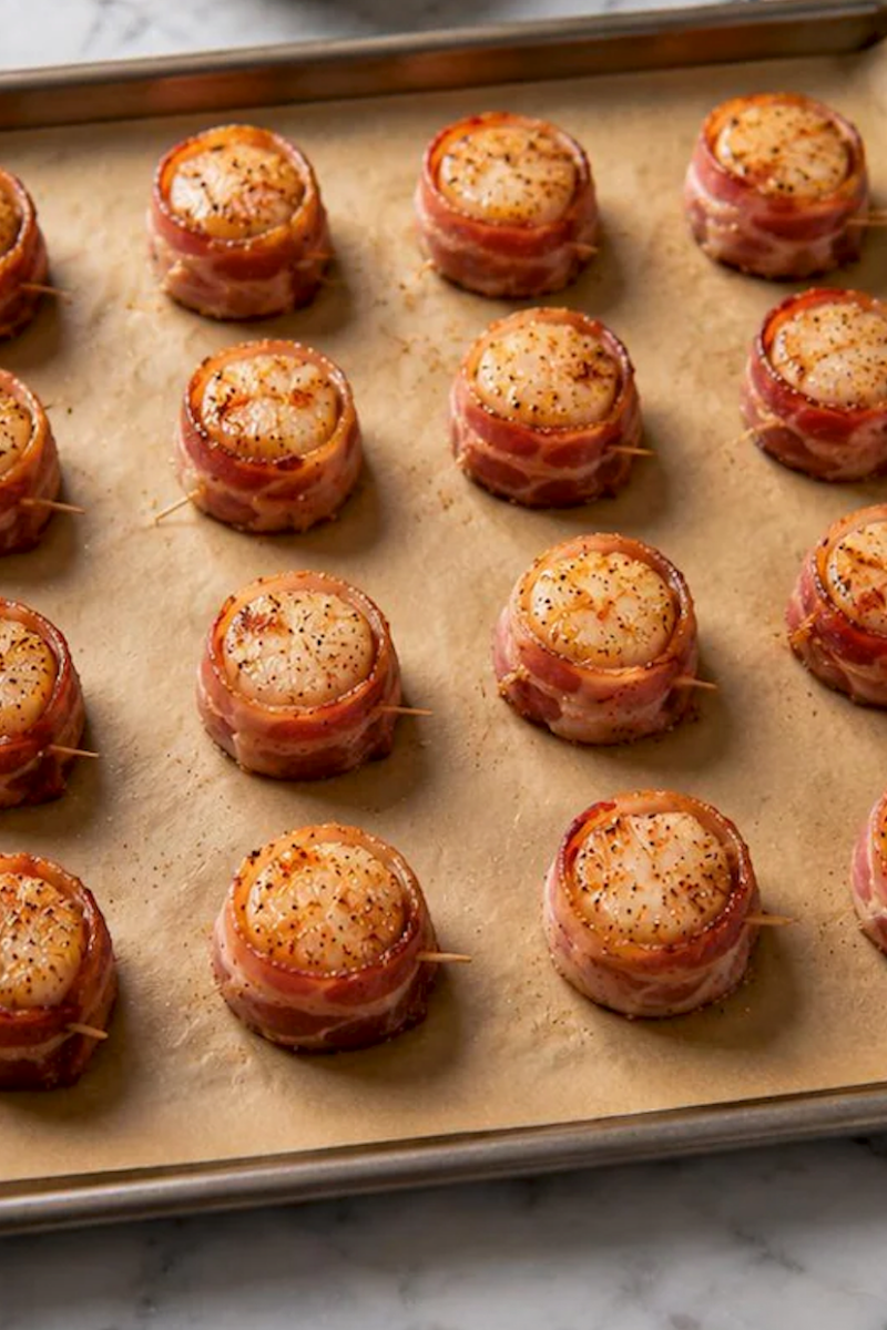 Bacon wrapped scallops arranged evenly on a baking sheet before cooking