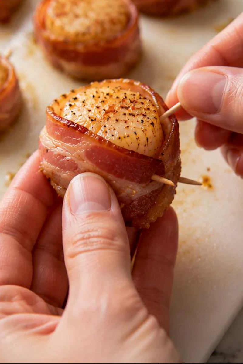Bacon being wrapped around a seasoned sea scallop and secured with a toothpick