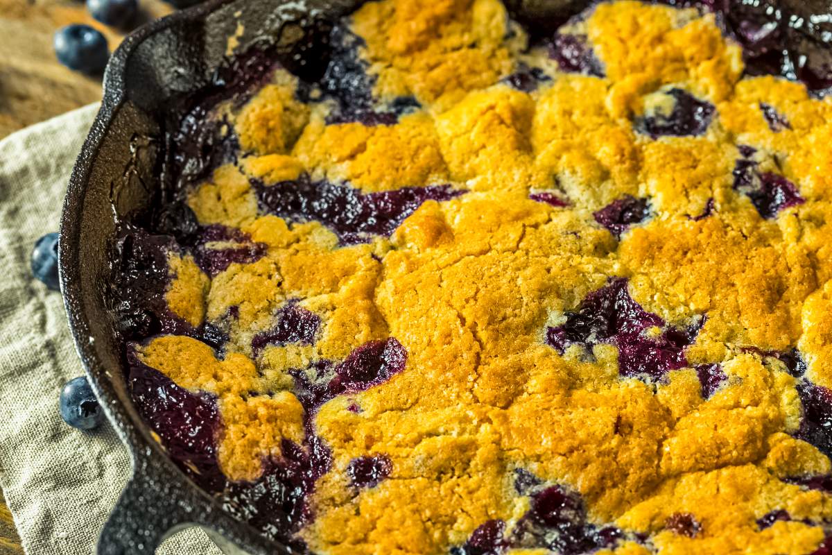 Close-up of blueberry cobbler with golden crust and bubbling juicy blueberry filling in cast iron skillet