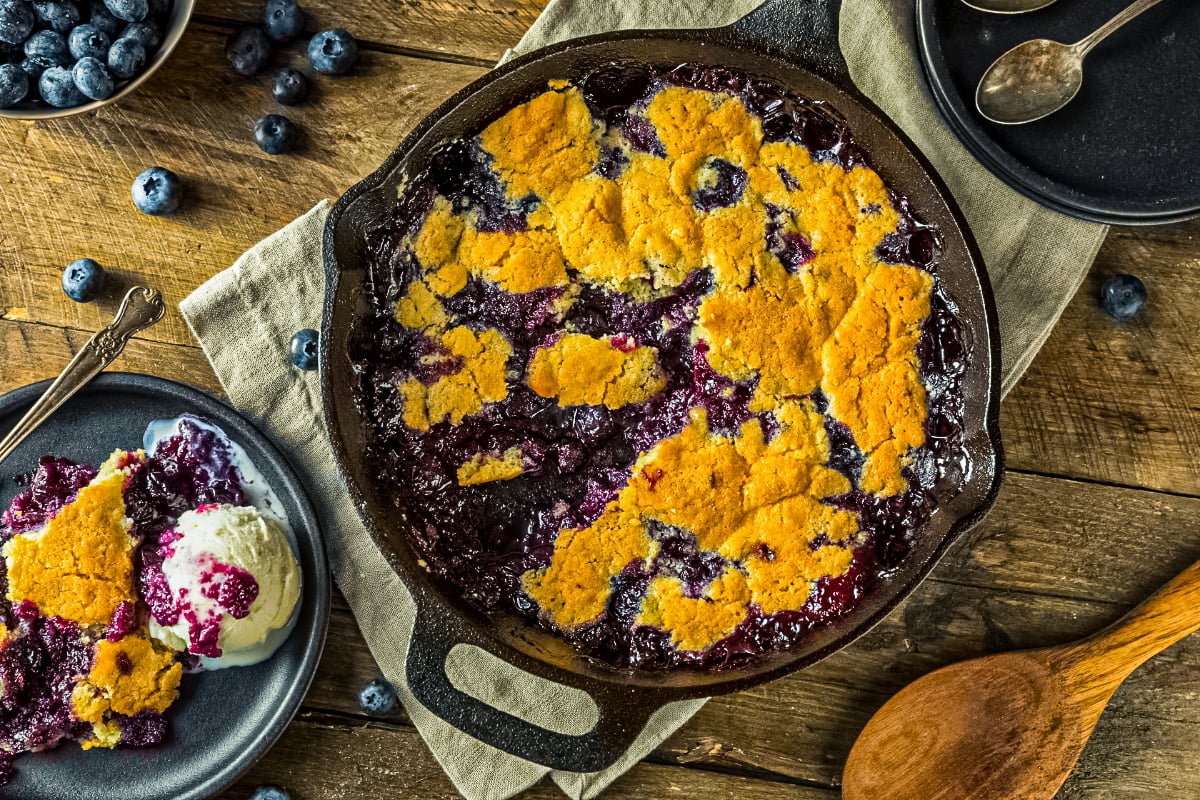 Easy blueberry cobbler in cast iron skillet with golden crust and bubbling blueberry filling, served with vanilla ice cream