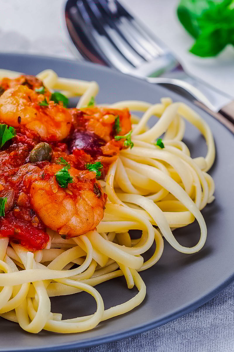 Shrimp linguine puttanesca in a white bowl topped with fresh parsley and lemon zest