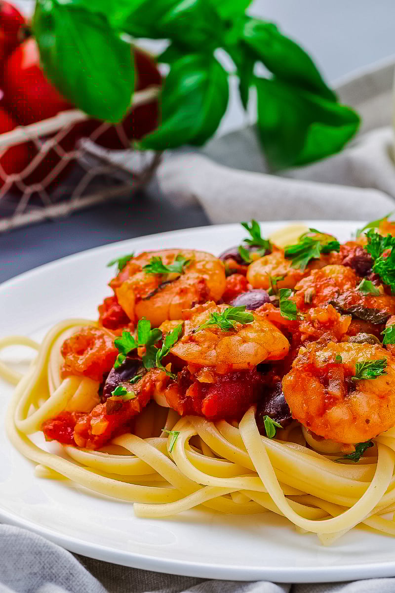 Shrimp linguine puttanesca in a white bowl topped with fresh parsley and lemon zest