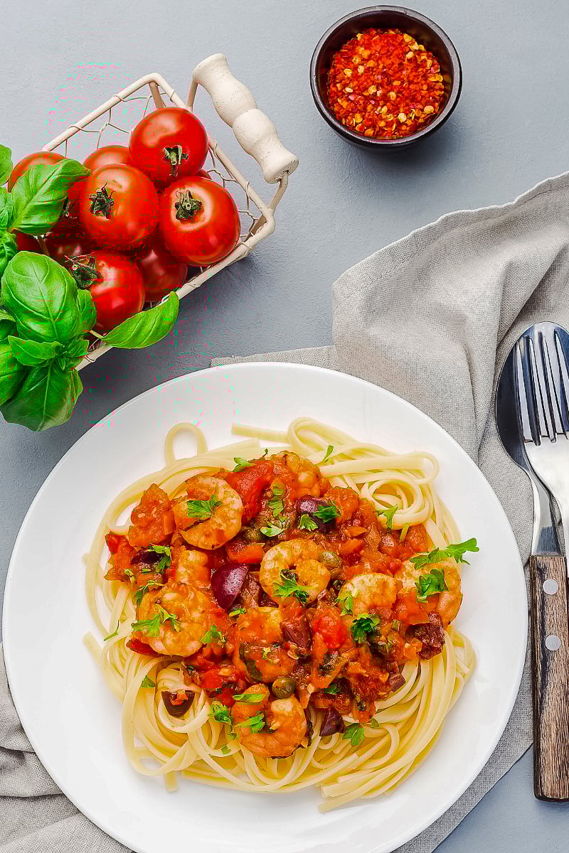 Shrimp linguine puttanesca in a white bowl topped with fresh parsley and lemon zest