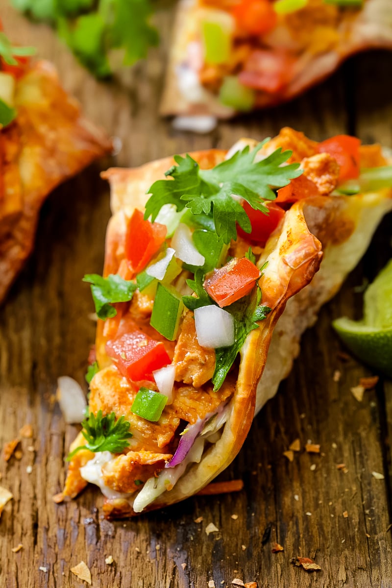 Crispy wonton tacos filled with spicy soy-ginger chicken, colorful Asian slaw, and drizzled sriracha mayo on a wooden platter."