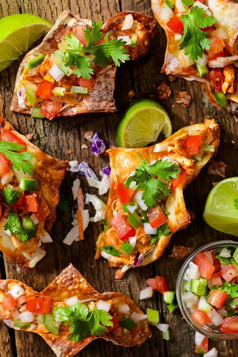 Crispy wonton tacos filled with spicy soy-ginger chicken, colorful Asian slaw, and drizzled sriracha mayo on a wooden platter."