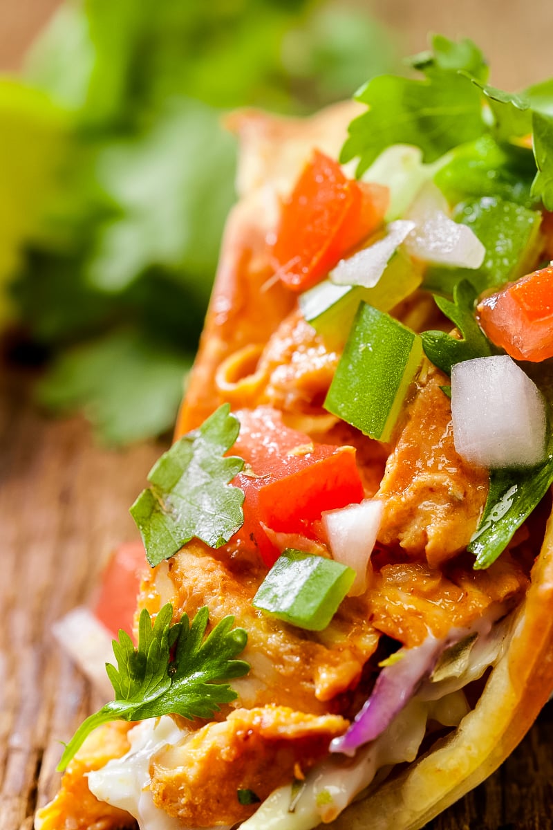 Crispy wonton tacos filled with spicy soy-ginger chicken, colorful Asian slaw, and drizzled sriracha mayo on a wooden platter."