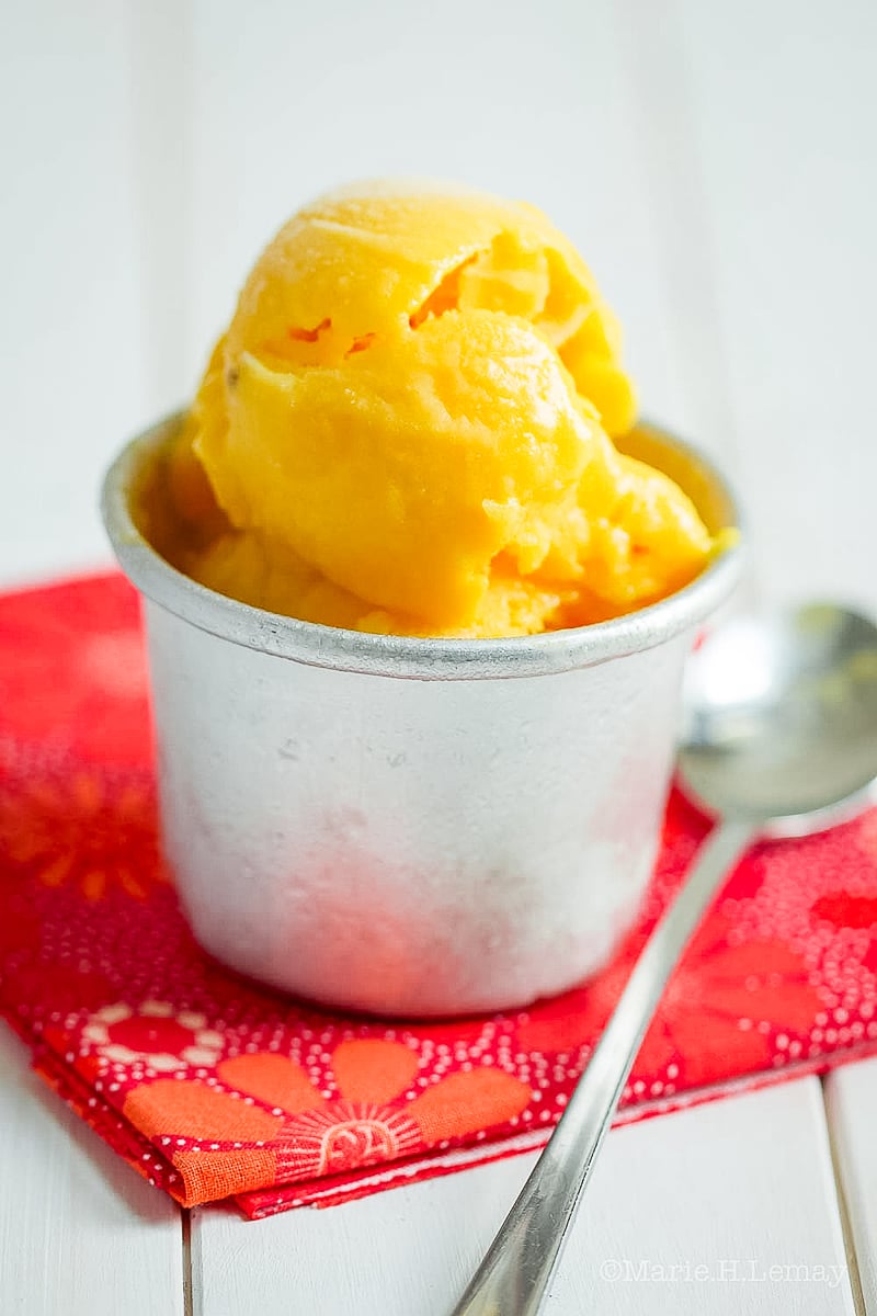 Scoops of homemade mango sorbet in a white bowl, garnished with mint and fresh mango slices.
