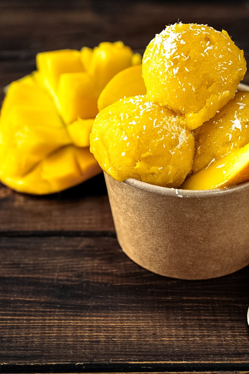 Scoops of homemade mango sorbet in a white bowl, garnished with mint and fresh mango slices.