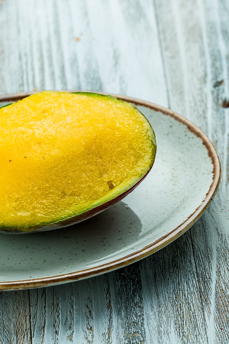 Scoops of homemade mango sorbet in a white bowl, garnished with mint and fresh mango slices.