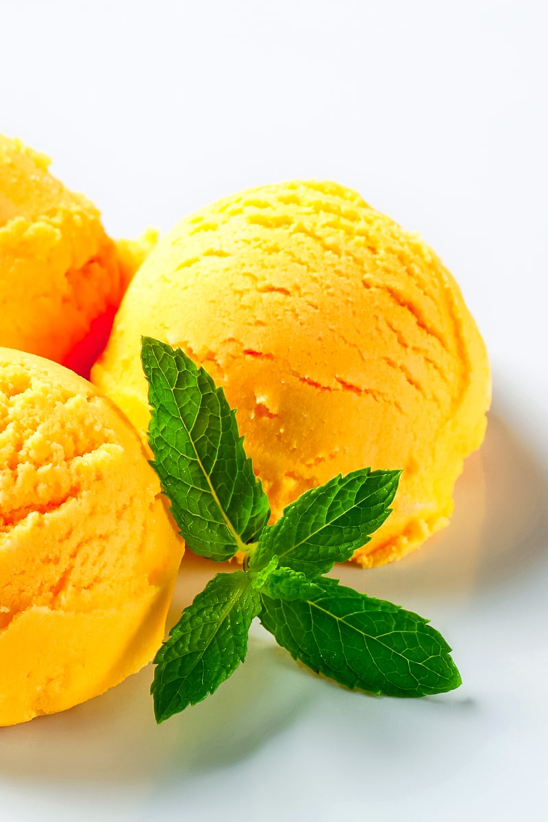 Scoops of homemade mango sorbet in a white bowl, garnished with mint and fresh mango slices.