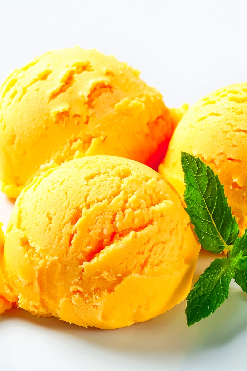 Scoops of homemade mango sorbet in a white bowl, garnished with mint and fresh mango slices.