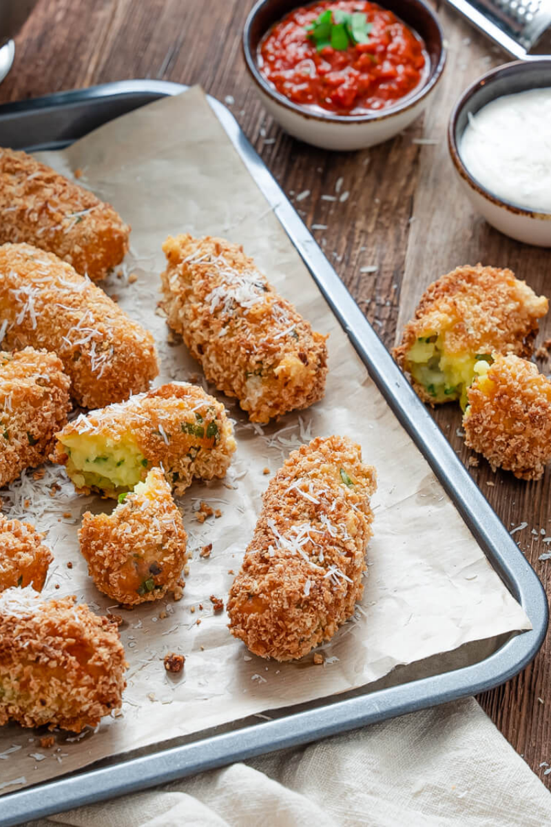 Golden brown mozzarella-stuffed potato croquettes served on a white plate with marinara sauce.