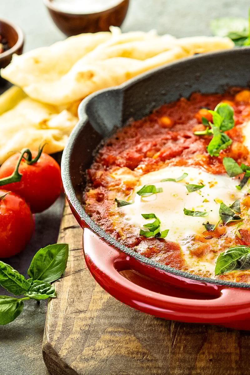 Shakshuka with Chickpeas in a skillet topped with poached eggs and fresh cilantro”