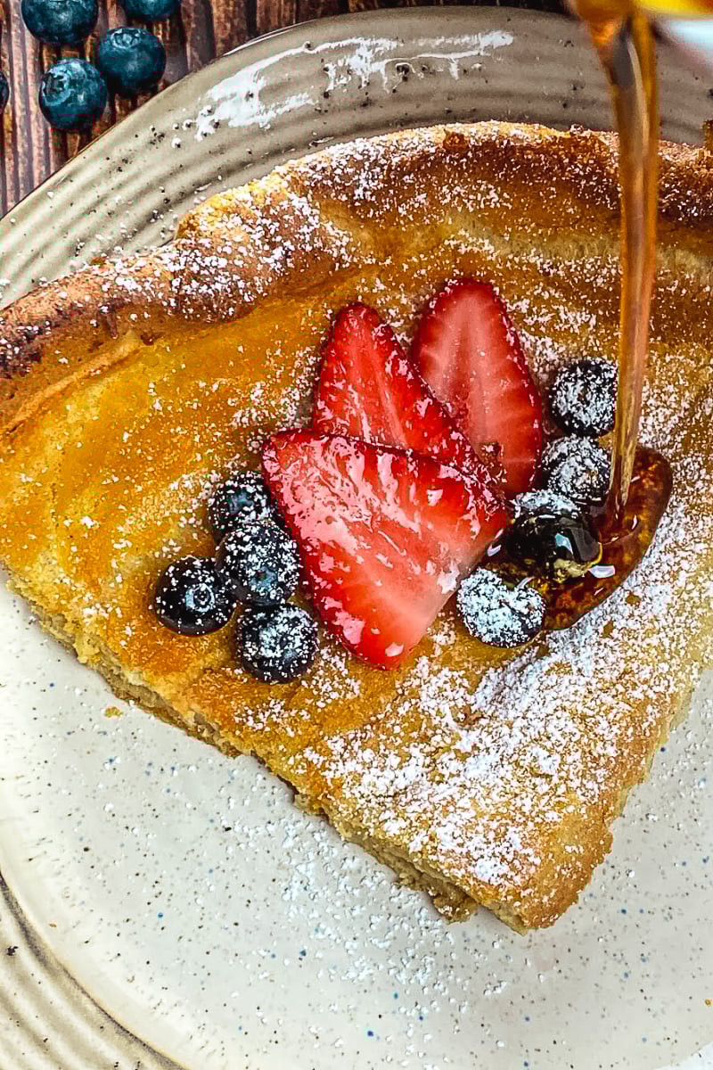 Golden Dutch Baby Pancake in cast iron skillet topped with fresh berries and powdered sugar"