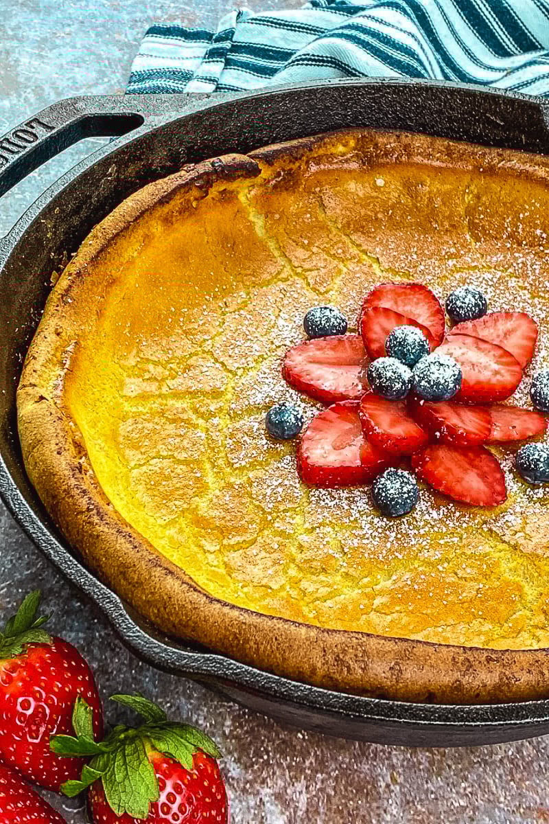Golden Dutch Baby Pancake in cast iron skillet topped with fresh berries and powdered sugar"