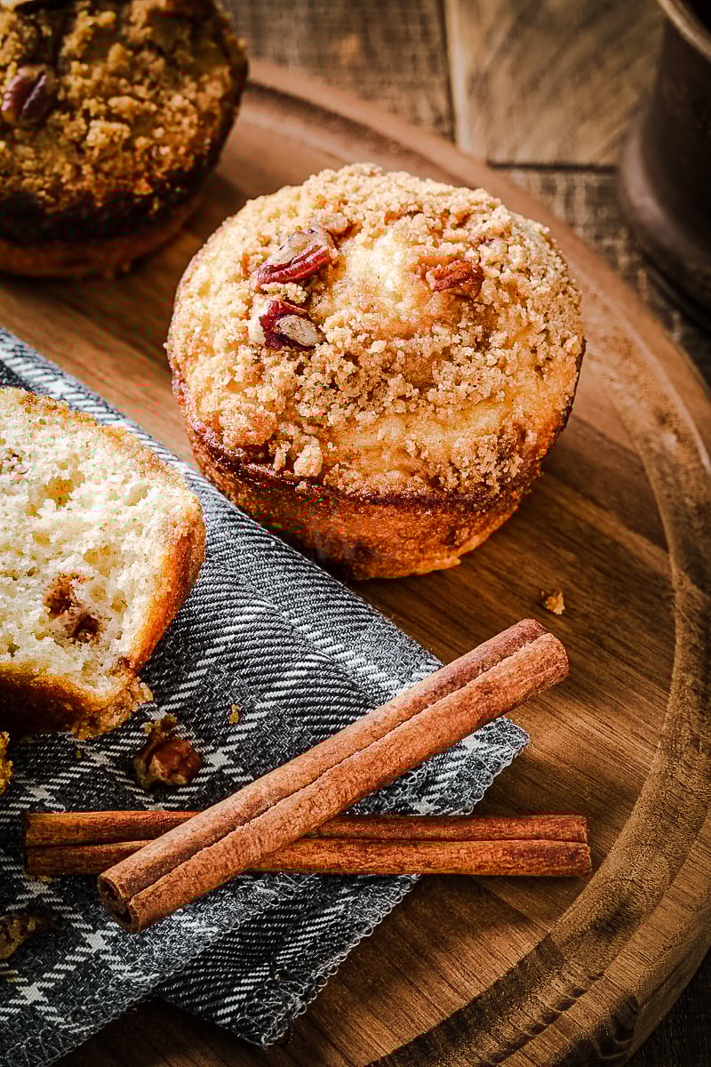 Close-up of cinnamon streusel nut muffins with pecan topping in a bowl, garnished with cinnamon sticks on a napkin