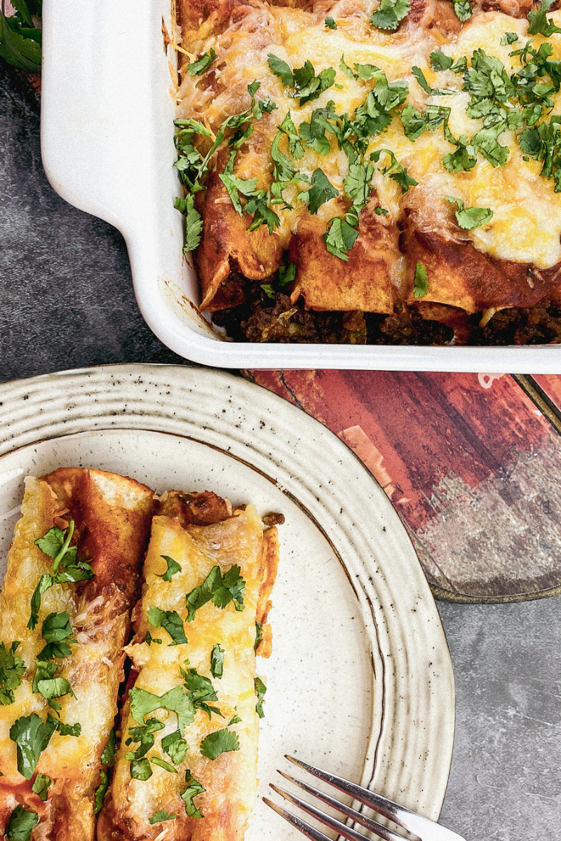 A baking dish filled with golden, cheesy beef enchiladas topped with fresh cilantro and avocado.