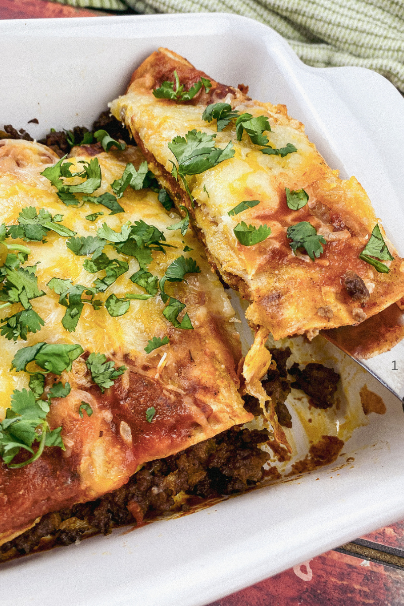 A baking dish filled with golden, cheesy beef enchiladas topped with fresh cilantro and avocado.