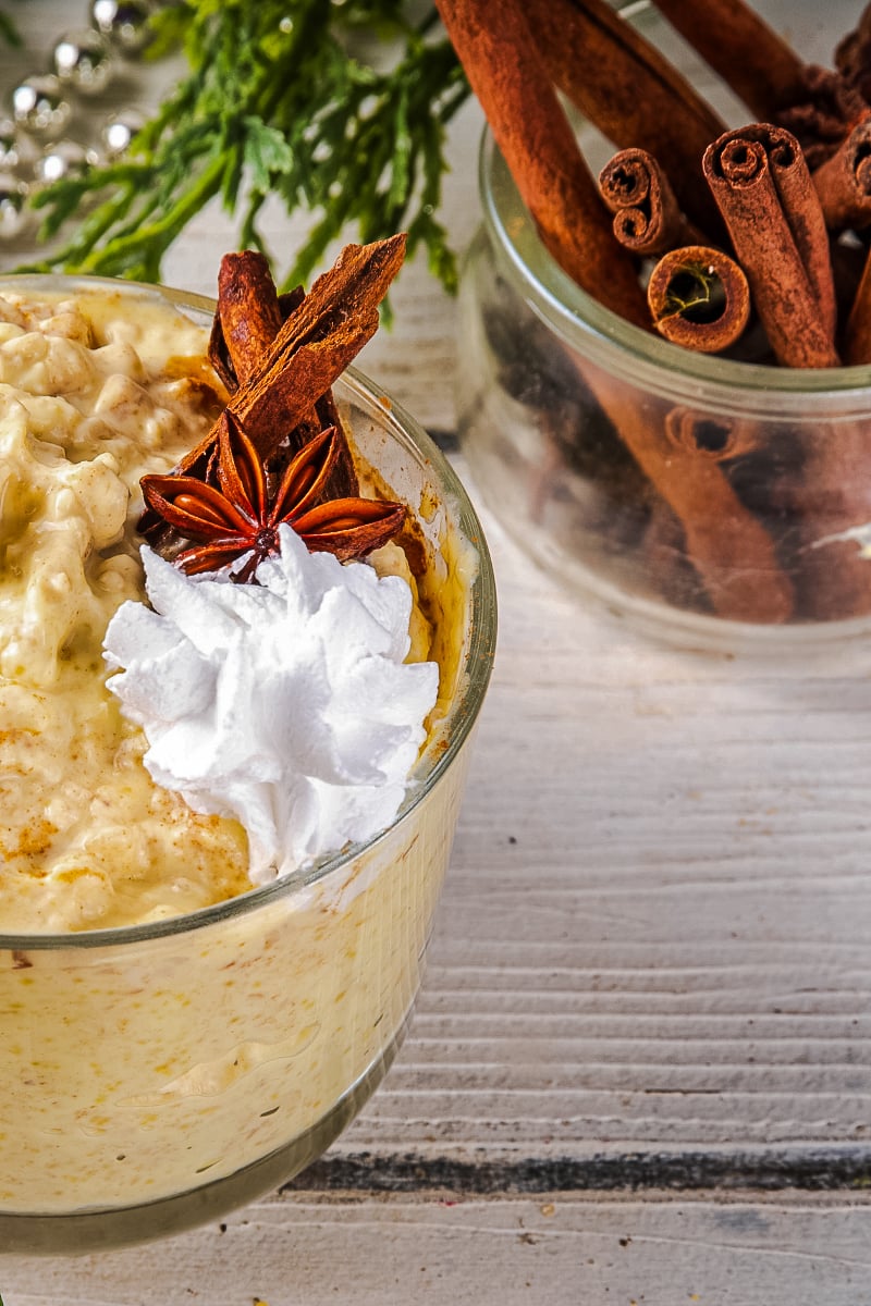 "Festive mason jar of Christmas eggnog overnight oats with cranberries, pecans, holiday spices, and a dusting of nutmeg on a wooden table with evergreen accents and cinnamon sticks."