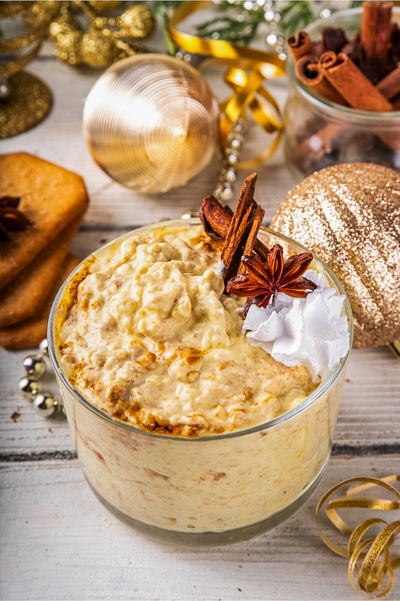 "Festive mason jar of Christmas eggnog overnight oats with cranberries, pecans, holiday spices, and a dusting of nutmeg on a wooden table with evergreen accents and cinnamon sticks."