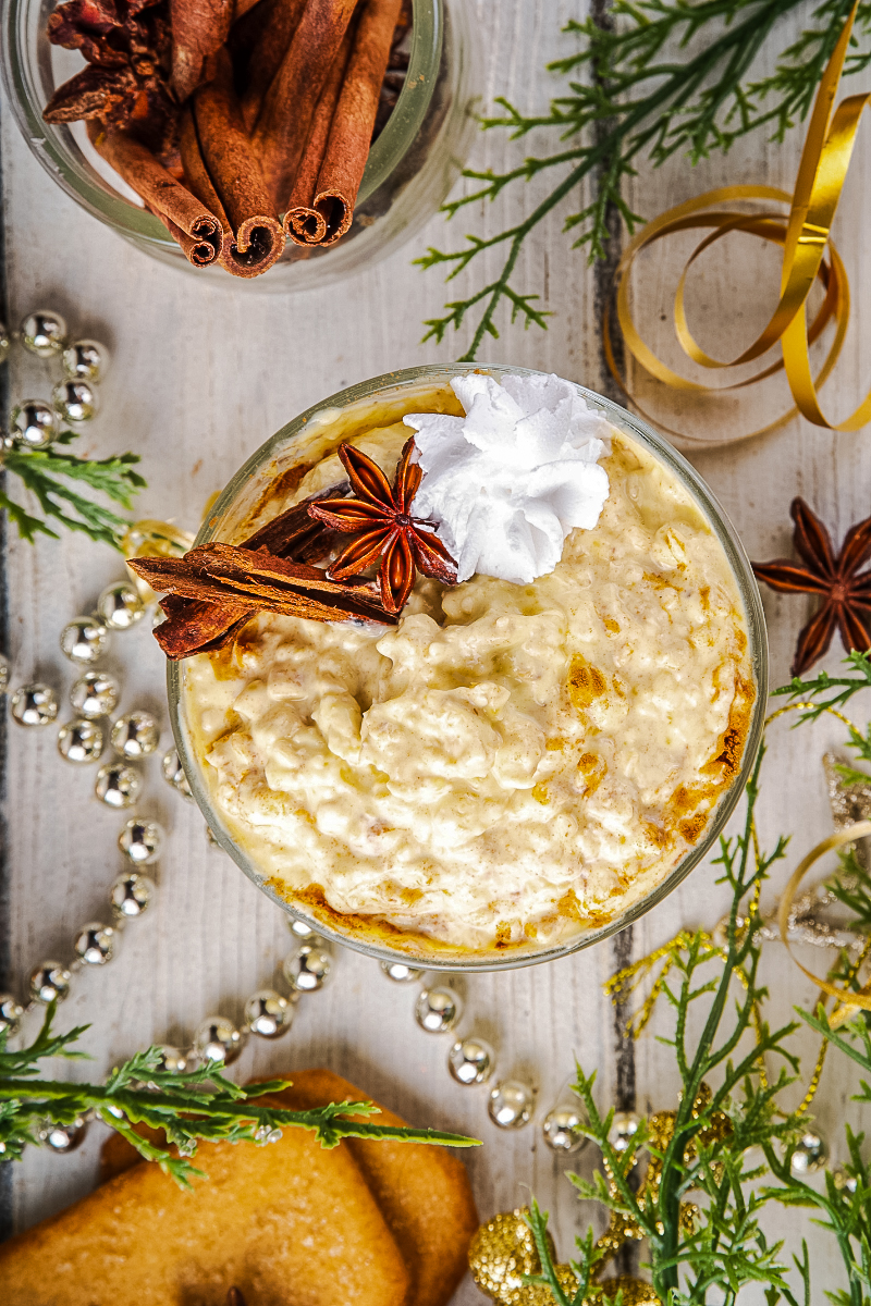 "Festive mason jar of Christmas eggnog overnight oats with cranberries, pecans, holiday spices, and a dusting of nutmeg on a wooden table with evergreen accents and cinnamon sticks."