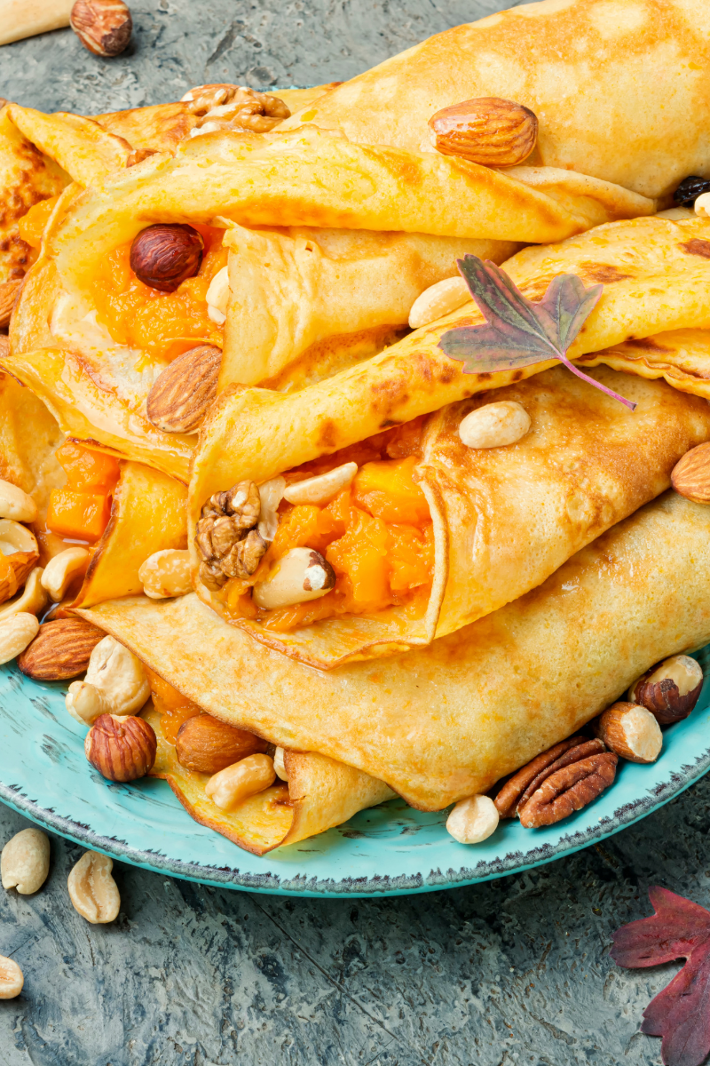 Stack of pumpkin-stuffed pancakes with cream cheese filling, drizzled with maple syrup and sprinkled with toasted pecans, dusted with cinnamon