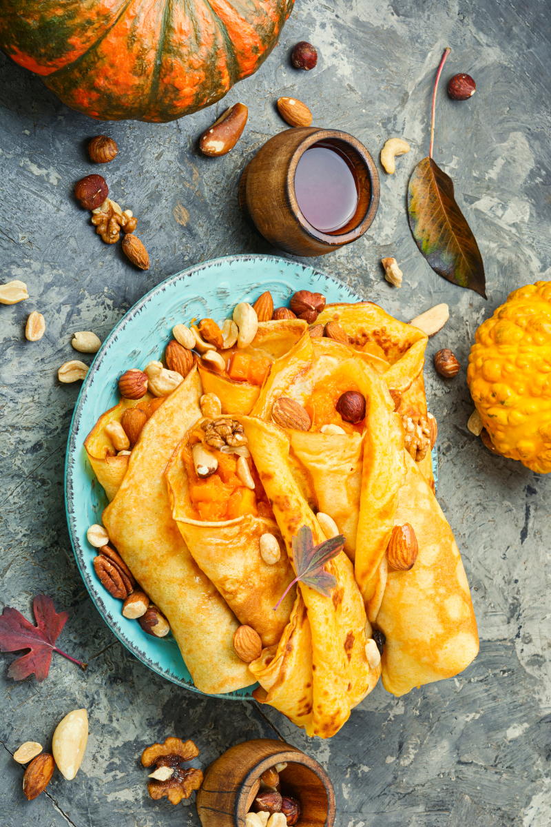 Stack of pumpkin-stuffed pancakes with cream cheese filling, drizzled with maple syrup and sprinkled with toasted pecans, dusted with cinnamon