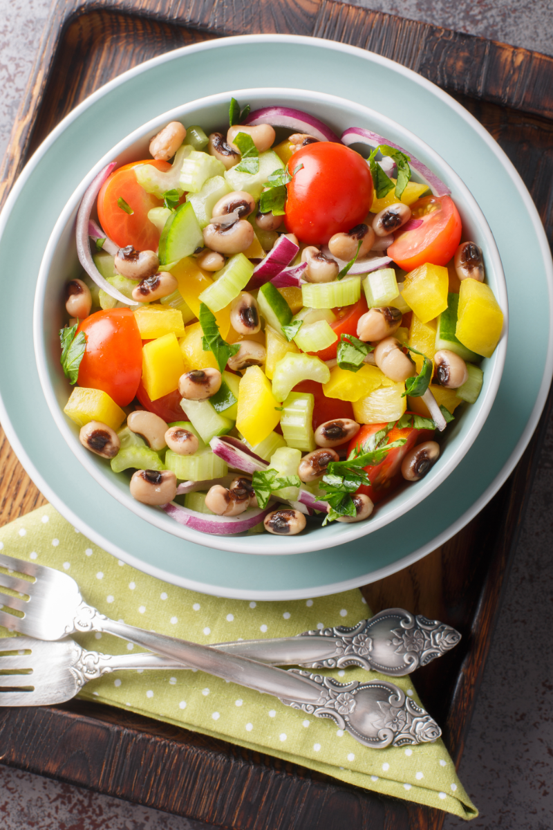 Mediterranean-style black-eyed pea and vegetable salad served in a clear glass bowl with fresh herbs on top
