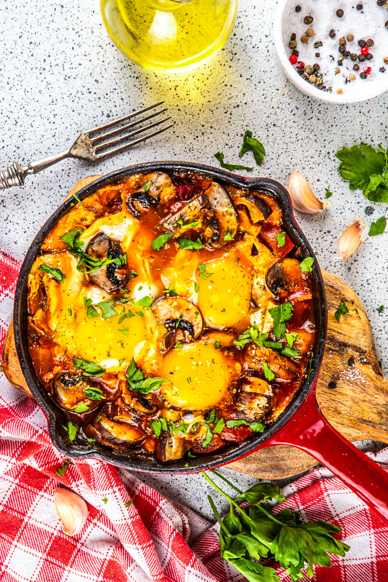 Mushroom shakshuka with baked eggs in a cast iron skillet, garnished with fresh parsley