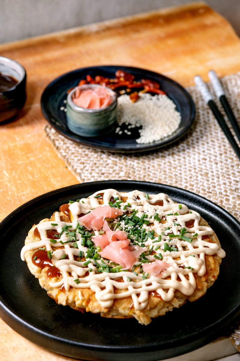 Japanese cabbage pancake Okonomiyaki served hot on a white plate with drizzled Japanese mayo and okonomiyaki sauce