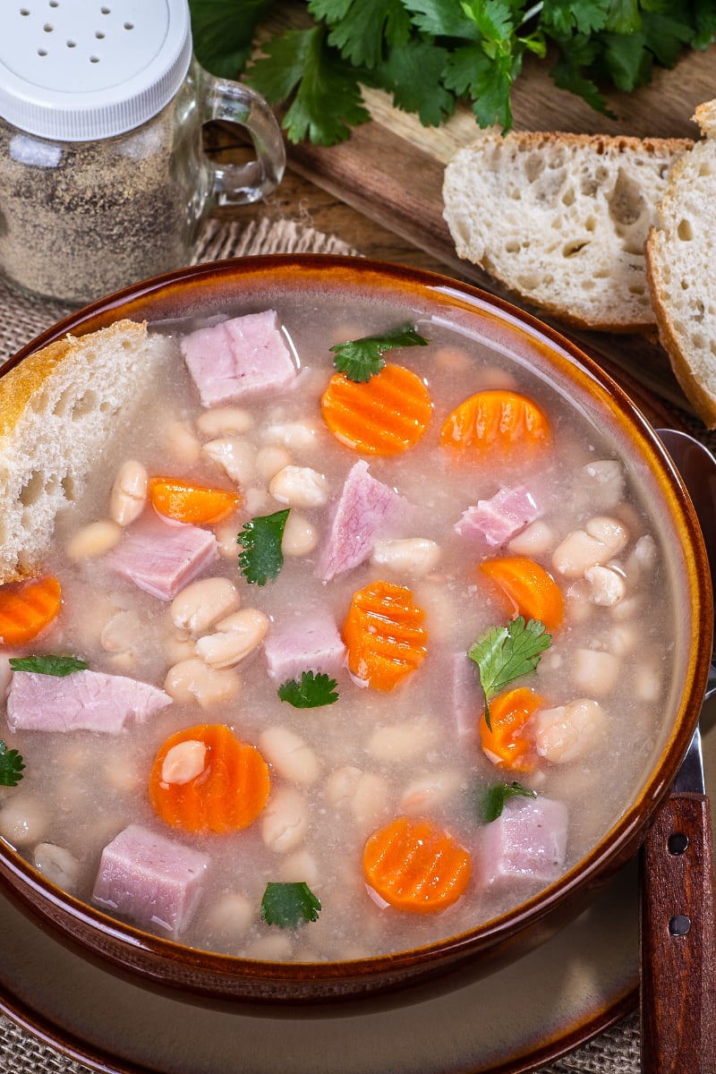 Bowl of healthy white bean and ham soup topped with fresh parsley, showing creamy beans and savory ham pieces