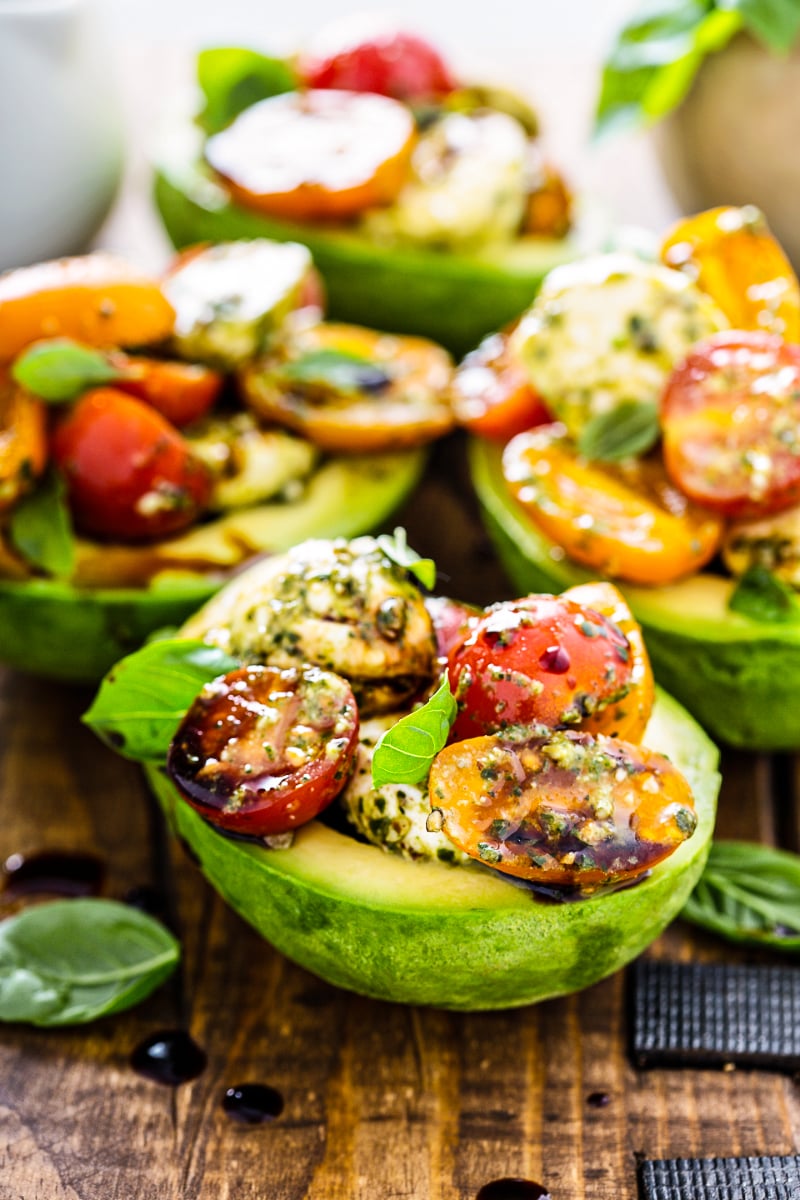 avocado stuffed with pesto caprese salad topped with mozzarella pearls cherry tomatoes basil and balsamic glaze