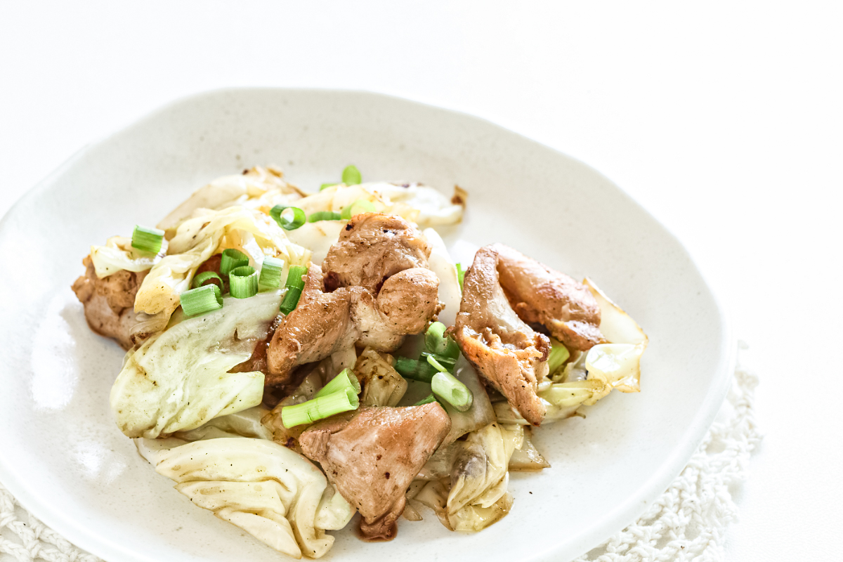 Pan-seared chicken with tender sautéed cabbage and garlic, garnished with fresh chopped green onions and served in a simple white bowl as a quick Korean-inspired skillet dinner.