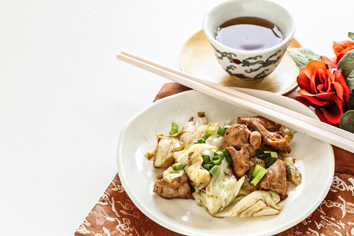 Korean-style chicken and sautéed cabbage served in a shallow bowl, topped with chopped green onions and paired with chopsticks and a small cup of tea for a simple Asian-inspired skillet meal.